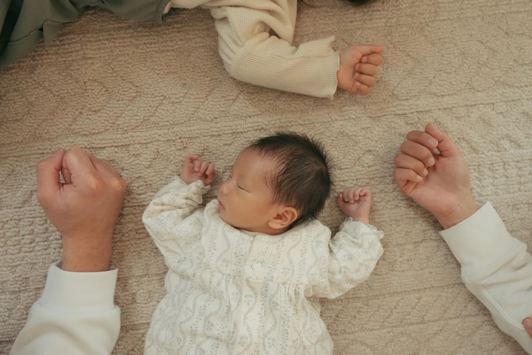 赤ちゃんの小さな体に家族の手が添えられた写真