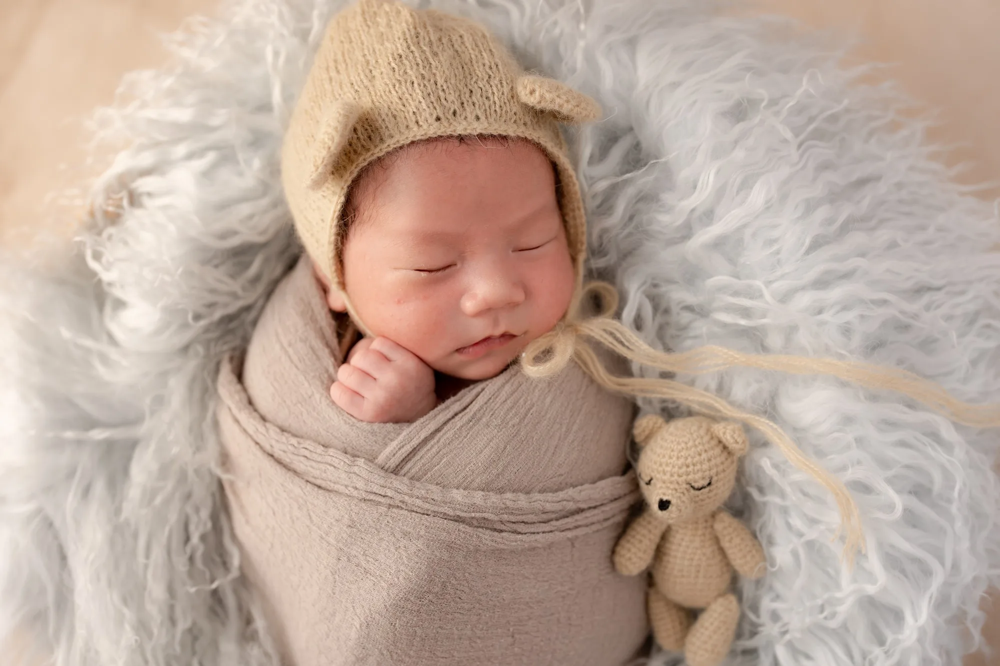 ニット帽をかぶり、小さなくまのそばで眠る赤ちゃん