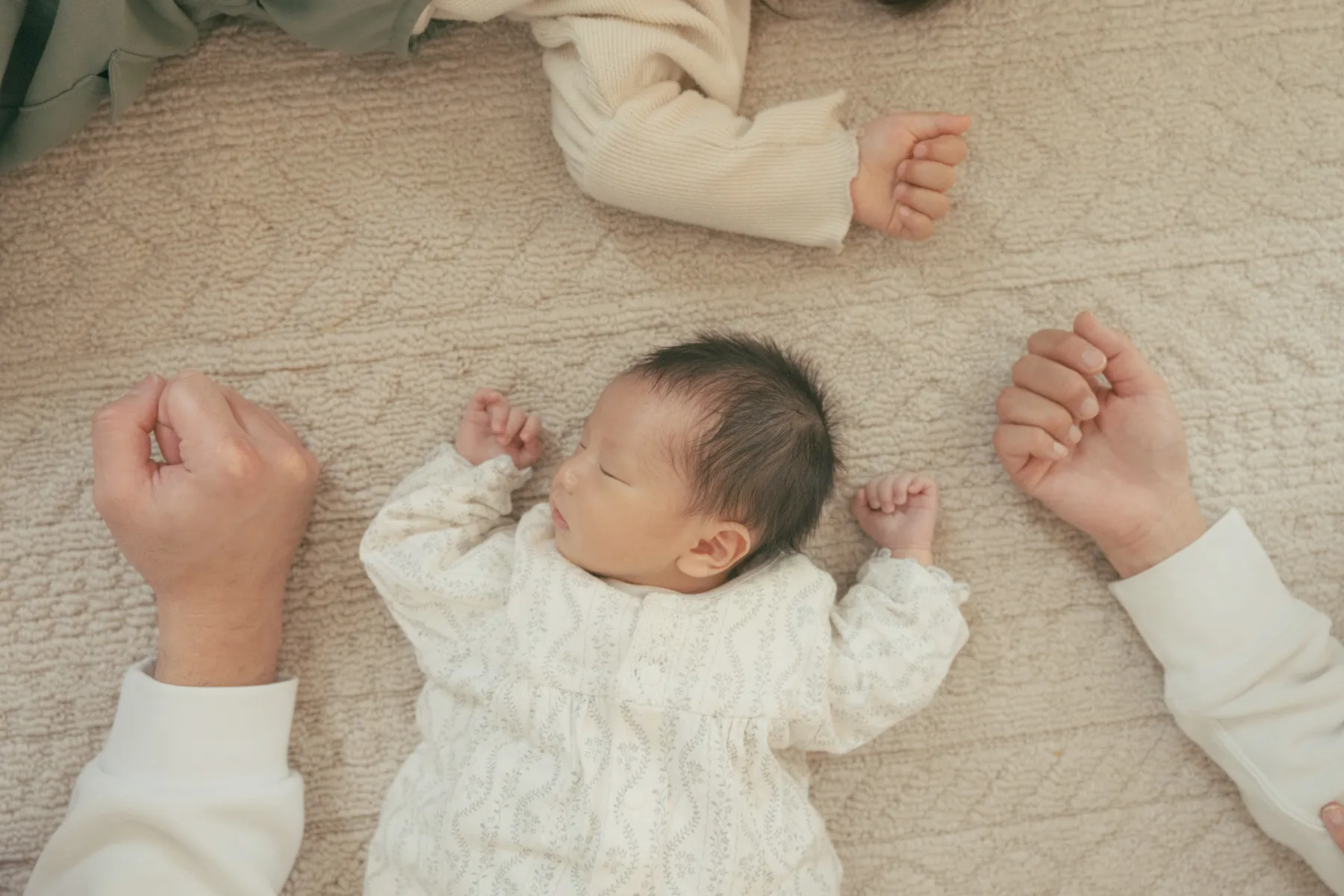 赤ちゃんの小さな体に家族の手が添えられた写真