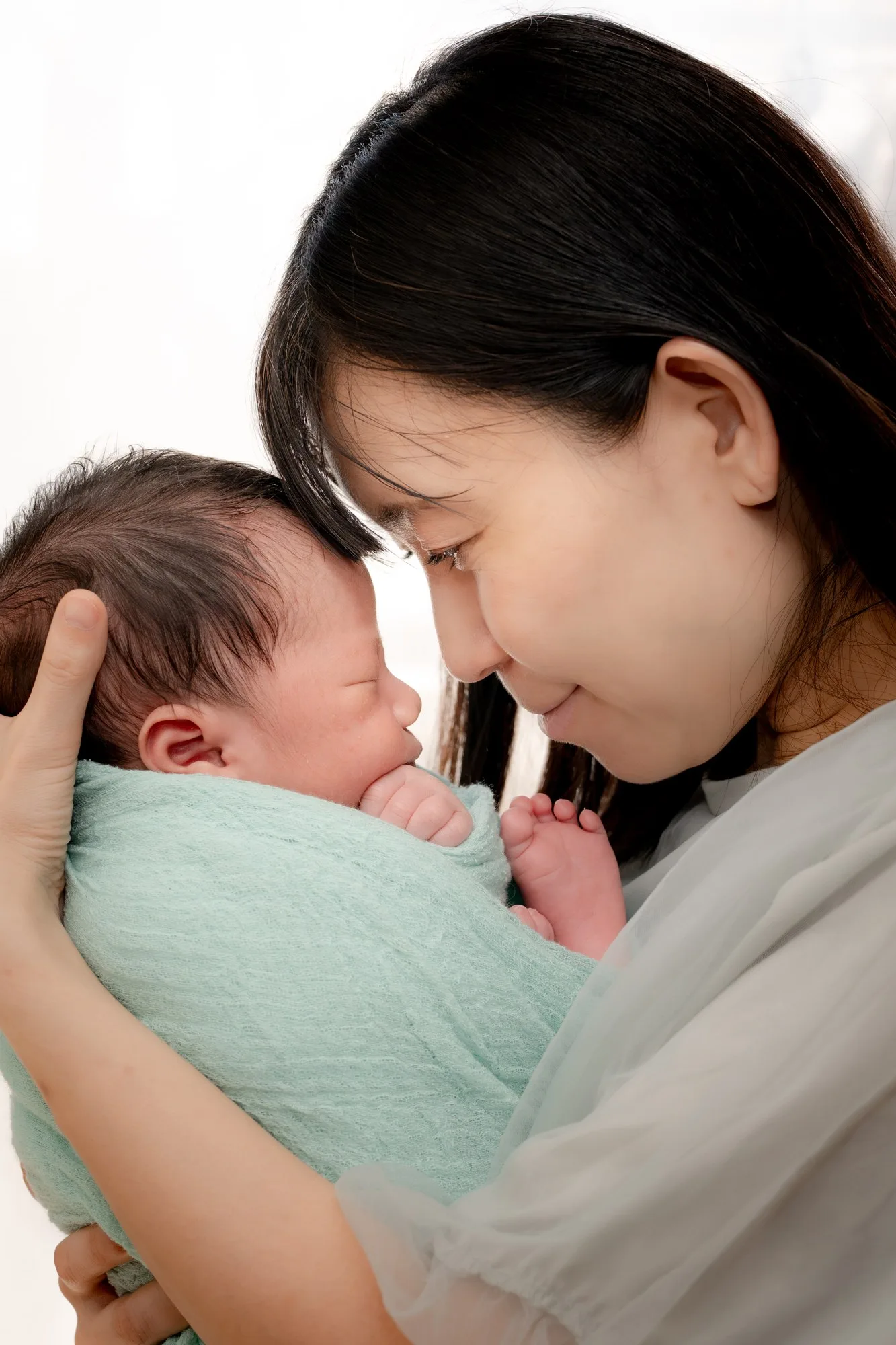 おくるみの赤ちゃんを支え、そっと額を寄せるお母さん
